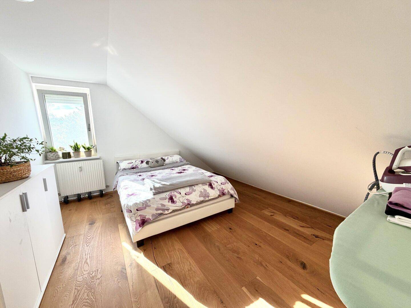 Schlafzimmer mit Doppelbett, weißen Schränken, Holzboden und einem Fenster, das viel Licht hereinlässt.