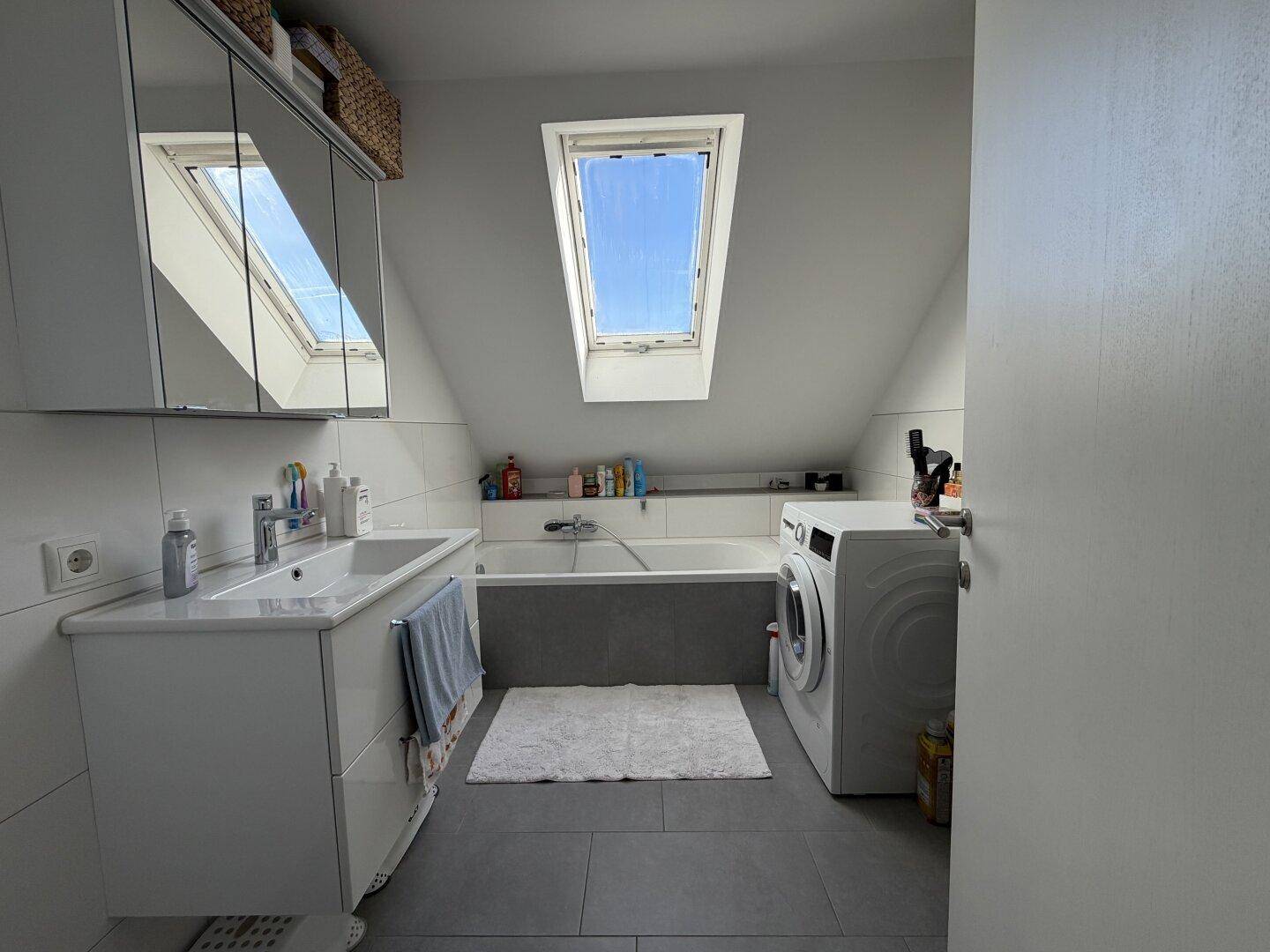 Modernes Badezimmer mit Badewanne, Waschbecken, Waschmaschine und großem Dachfenster in der Dachschräge.