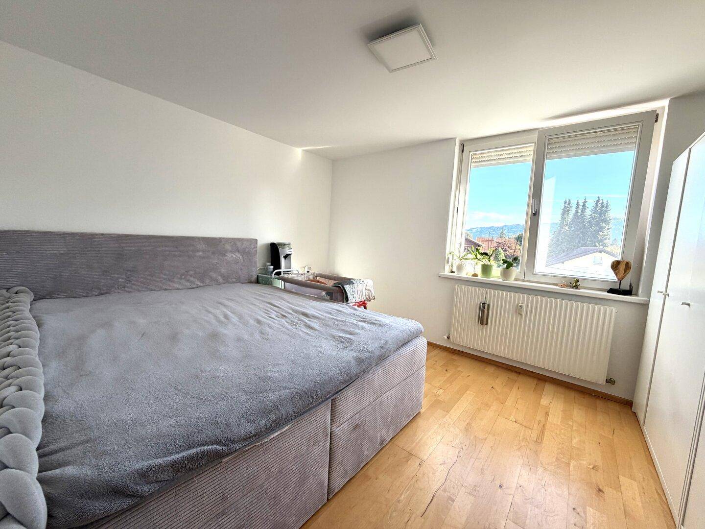 Helles Schlafzimmer mit großem Bett, Fenster und Holzboden, bietet eine angenehme Wohnatmosphäre.