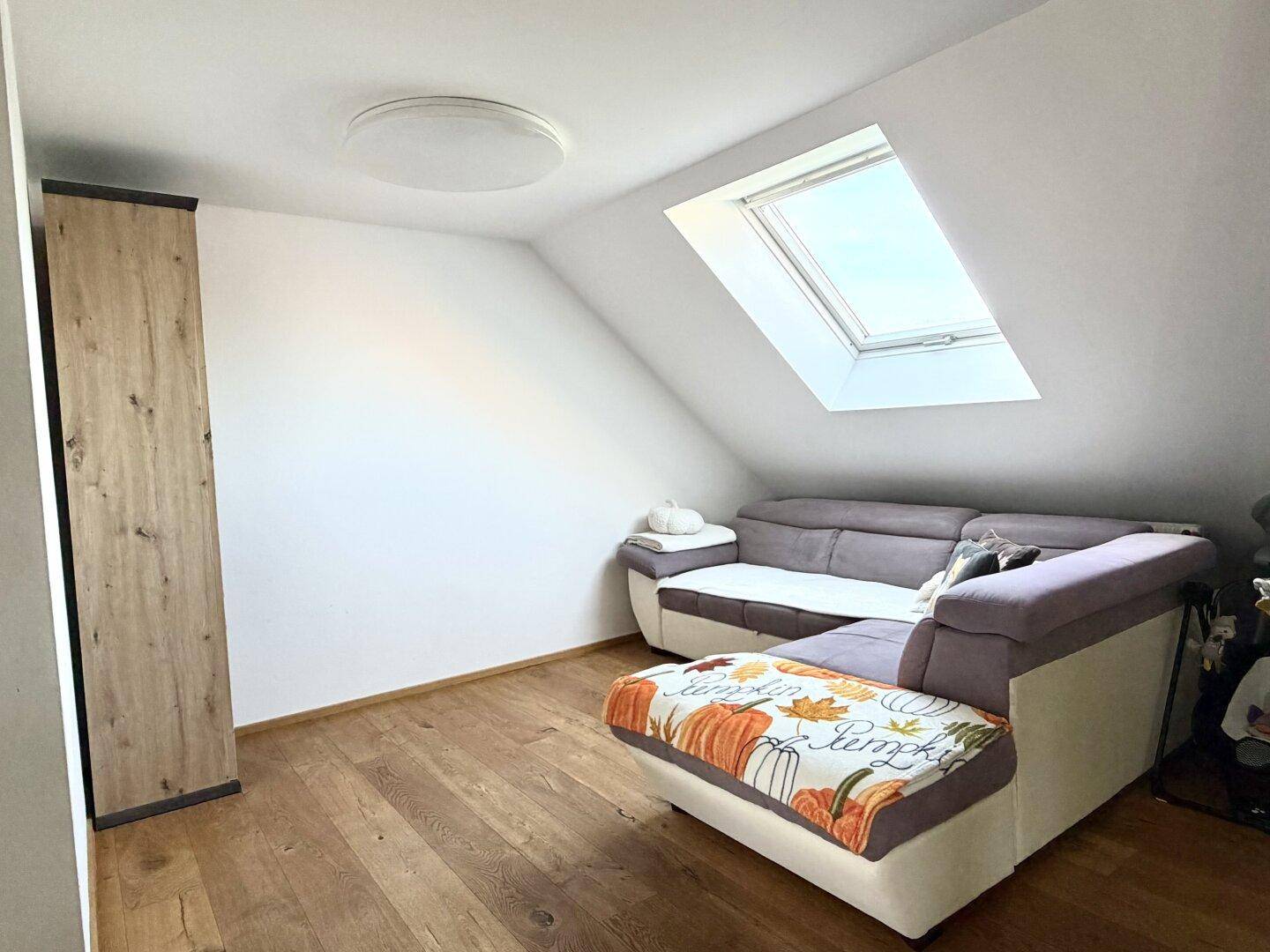 Gemütliches Wohnzimmer mit Ecksofa, Holzboden und einem Dachfenster in der Dachschräge.