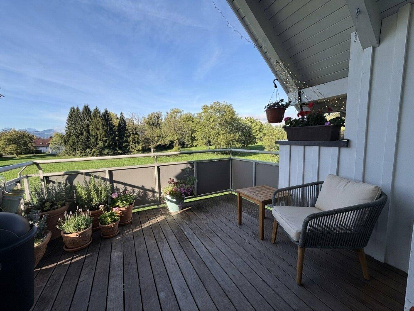 Gemütlicher Balkon mit Holzboden, Pflanzen und Sitzgelegenheiten, bietet einen schönen Blick ins Grüne.