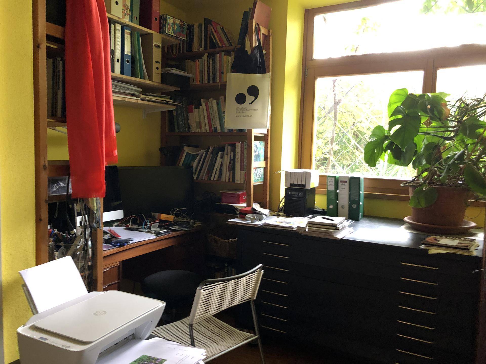 Gemütliches Arbeitszimmer mit gelben Wänden, Bücherregalen und einem Schreibtisch am Fenster.