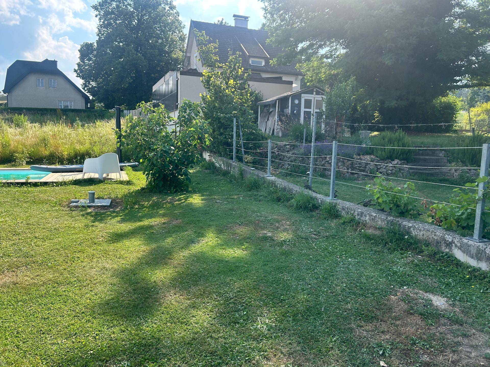 Blick auf den hinteren Gartenbereich mit üppiger Vegetation und dem Wohnhaus im Hintergrund.