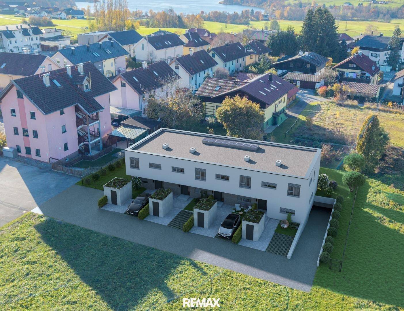 Luftaufnahme einer modernen Wohnanlage mit Reihenhäusern, Carports und Seeblick in ländlicher Umgebung.