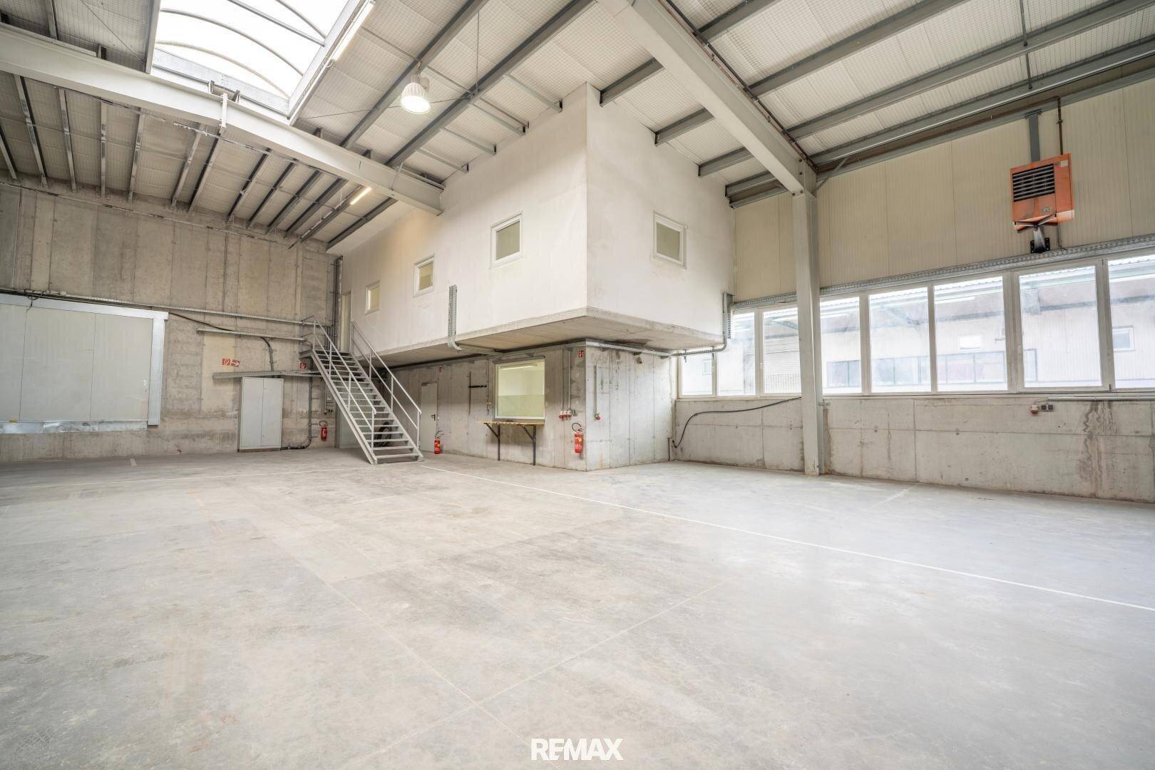 Helle Lagerhalle mit Betonboden, Oberlichtern und einer erhöhten Büro- oder Arbeitsplattform.
