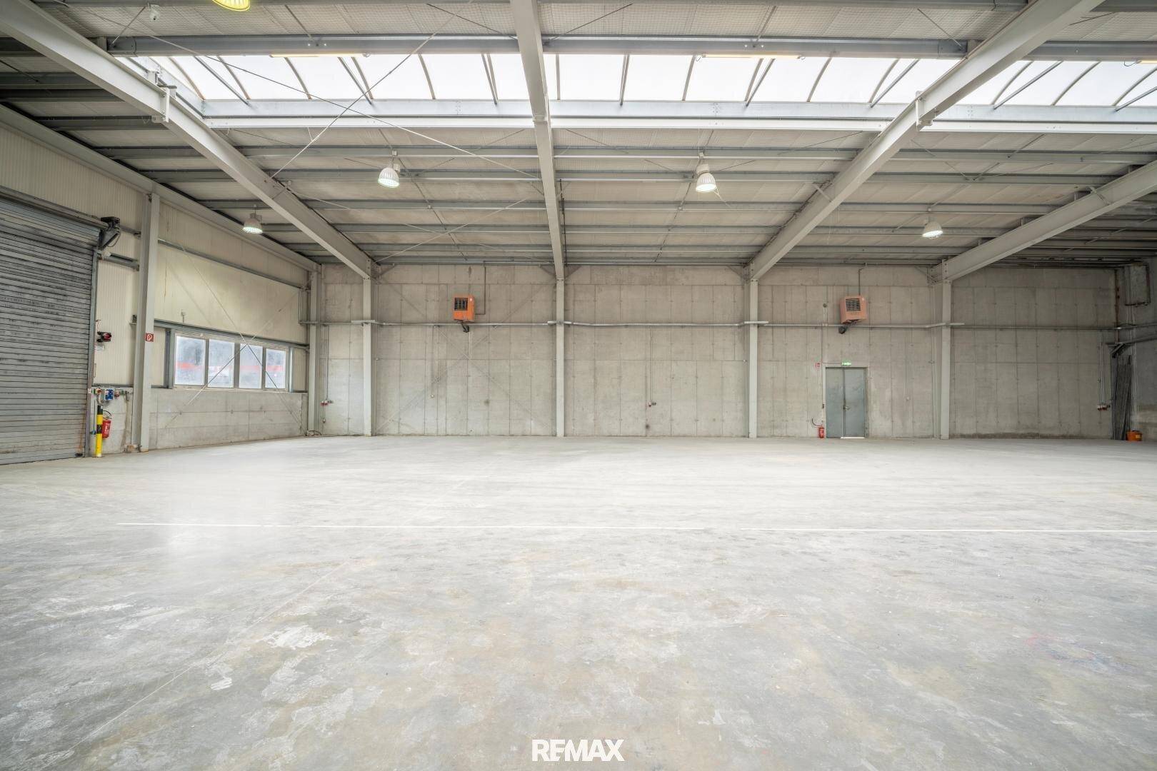 Geräumige Lagerhalle mit Betonboden, Rolltor und Oberlichtern, die viel Tageslicht hereinlassen.