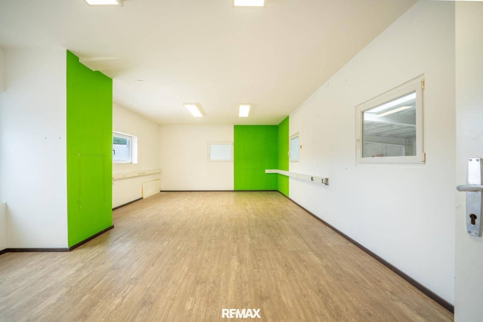 Moderner Büroraum mit Holzboden, weißen Wänden und einem Akzent in leuchtendem Grün.