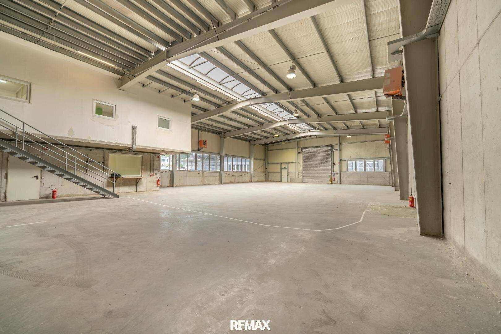 Weitläufige Lagerhalle mit Betonboden, Metallkonstruktion und Oberlichtern, bereit zur Nutzung.