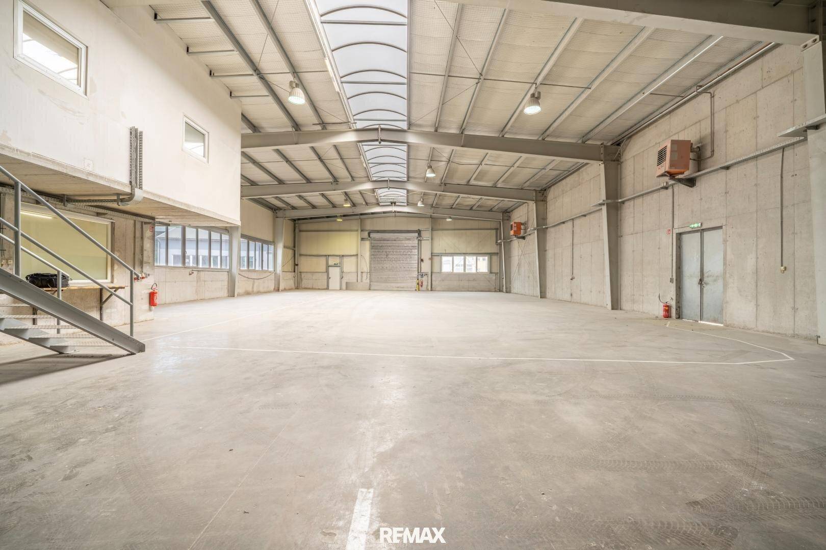 Geräumige, leere Lagerhalle mit hohen Decken, Betonboden und Oberlichtern für natürliches Licht.