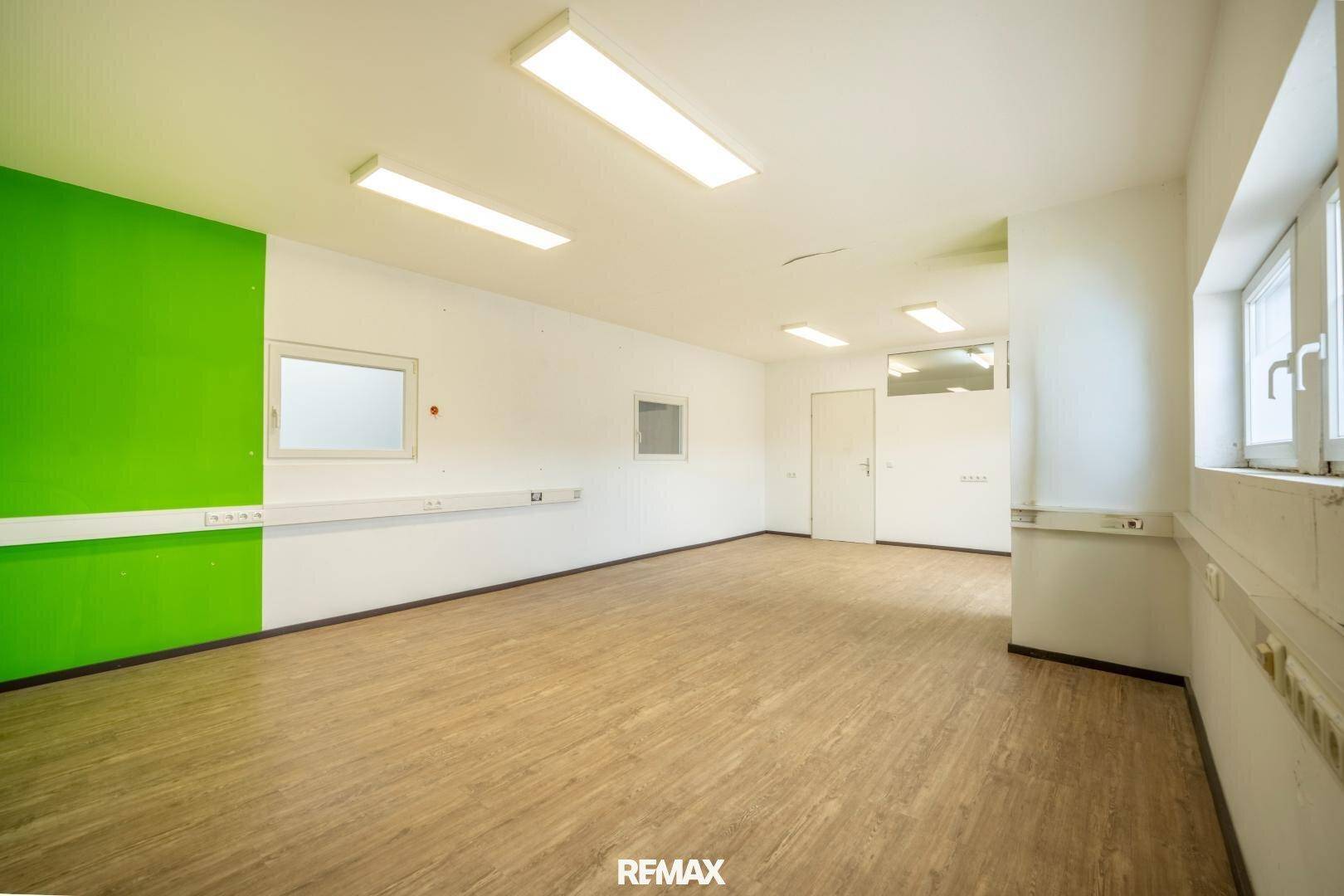 Heller Büroraum mit Laminatboden, weißen Wänden und einem grünen Akzentbereich.