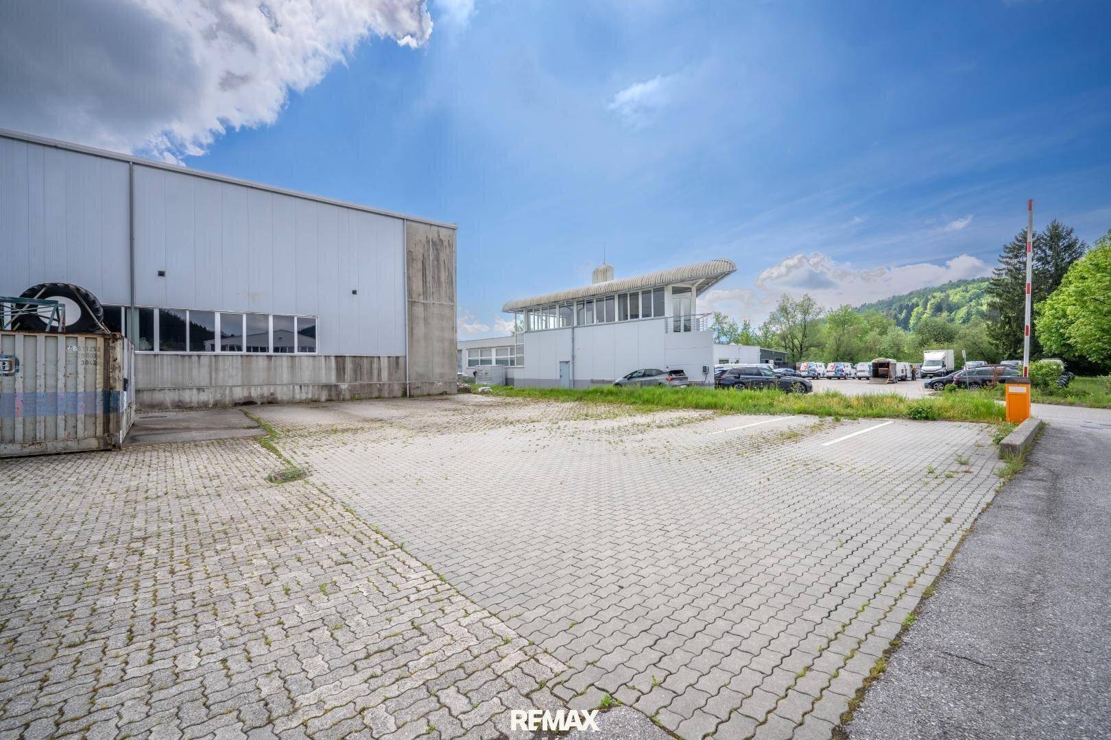 Weitläufiger Parkplatz mit Pflastersteinen und einer Zufahrtsschranke zum Gelände.