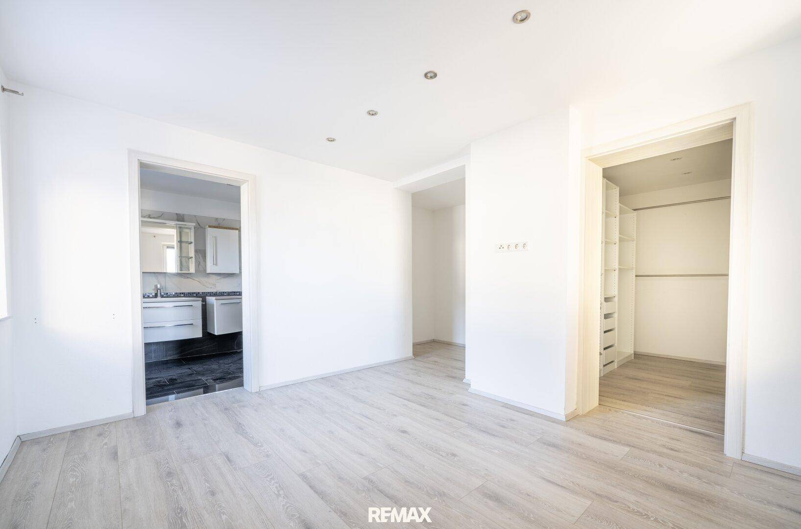 Heller Raum mit hellem Laminatboden, Zugang zu einem Badezimmer und einem begehbaren Kleiderschrank.