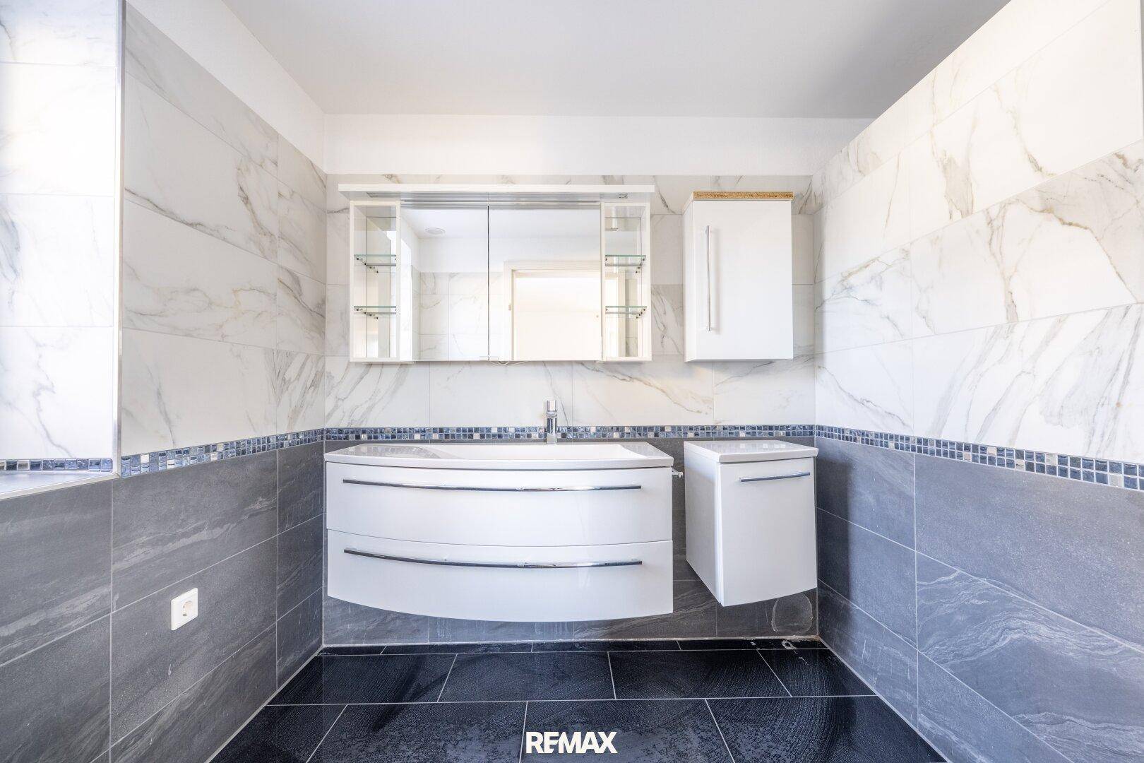 Modernes Badezimmer mit weißem Waschtisch, Spiegelschrank und eleganten Marmor-Optik-Fliesen.