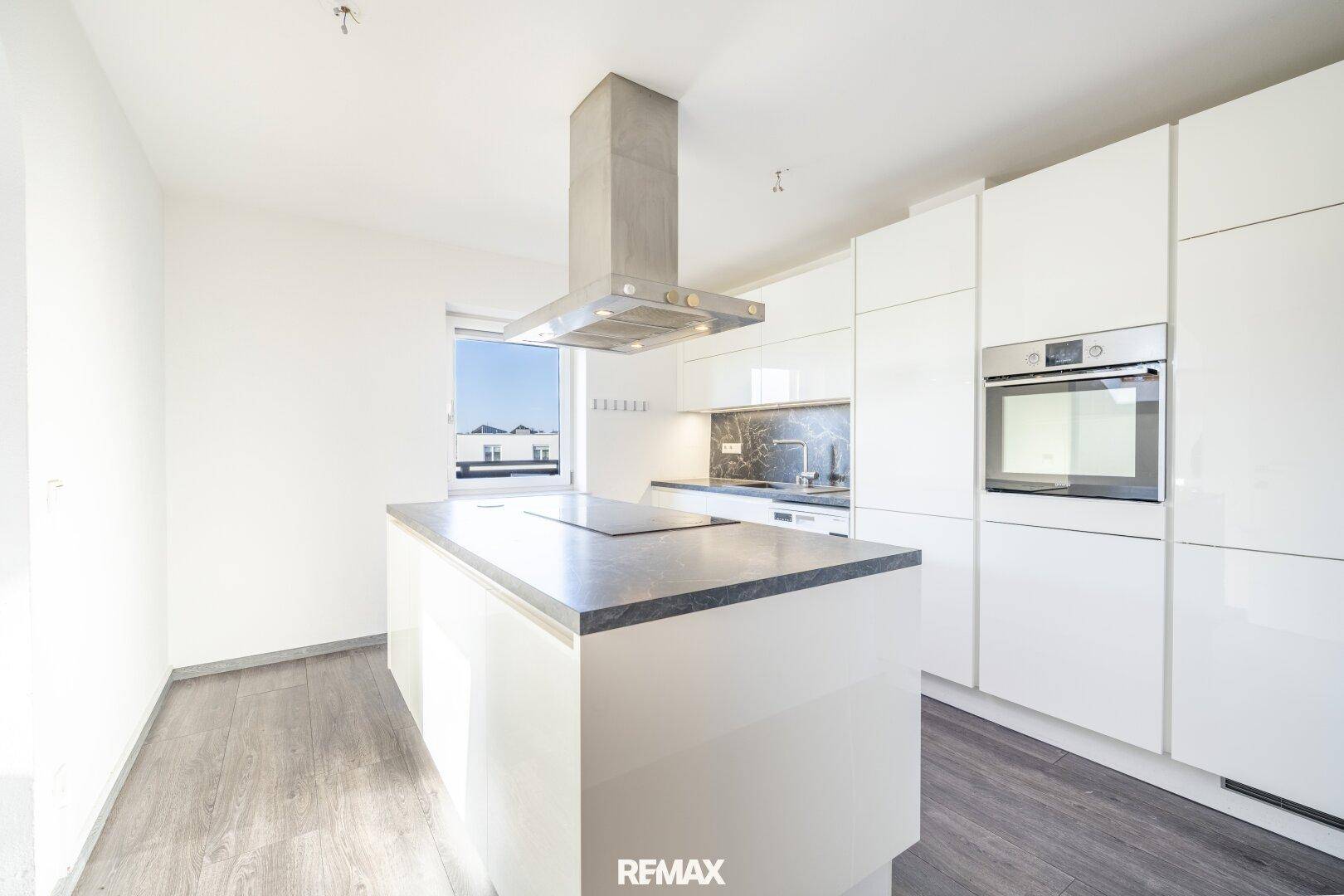 Moderne Küche mit weißen Hochglanzfronten, Kücheninsel mit Induktionskochfeld und integriertem Backofen.