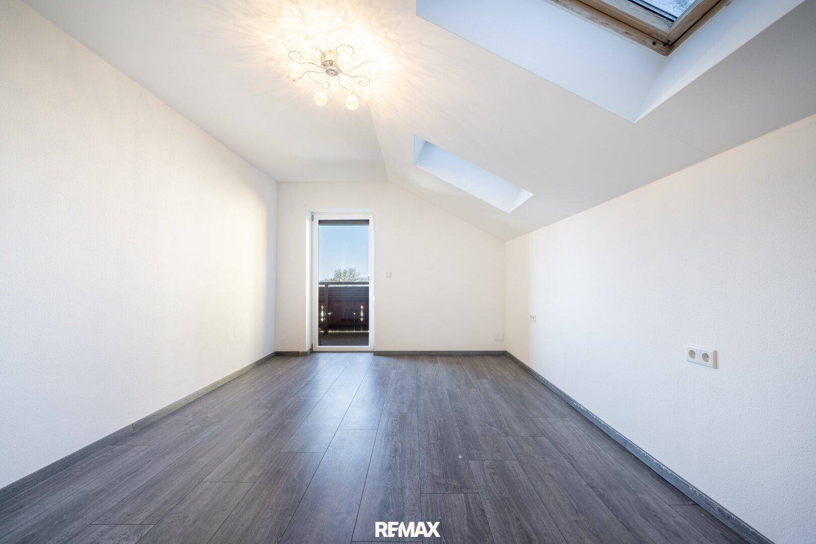 Heller Raum im Dachgeschoss mit Dachfenstern und Zugang zu einem kleinen Balkon.
