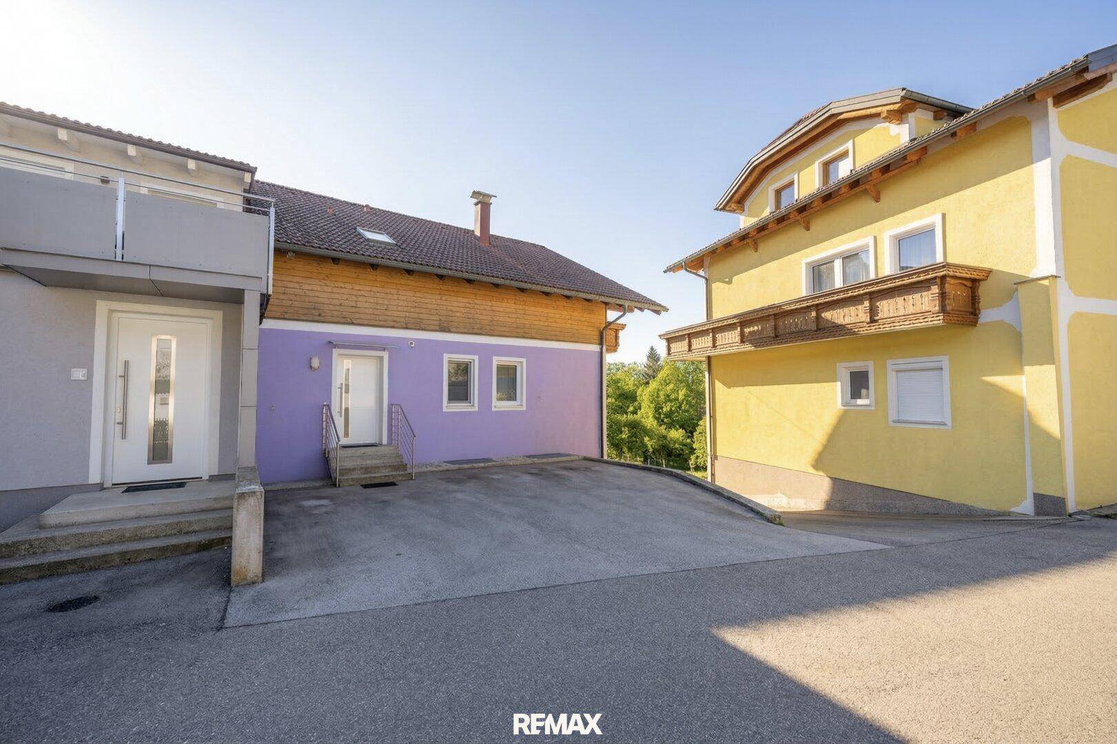 Außenansicht von zwei Häusern mit lila und gelber Fassade und einer gemeinsamen Auffahrt.