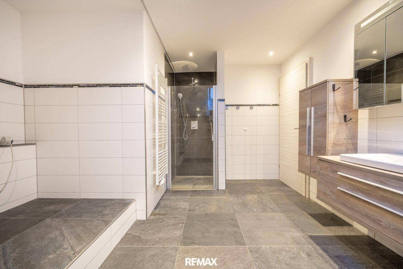 Geräumiges Badezimmer mit begehbarer Dusche, beheiztem Handtuchhalter und modernem Waschtisch.