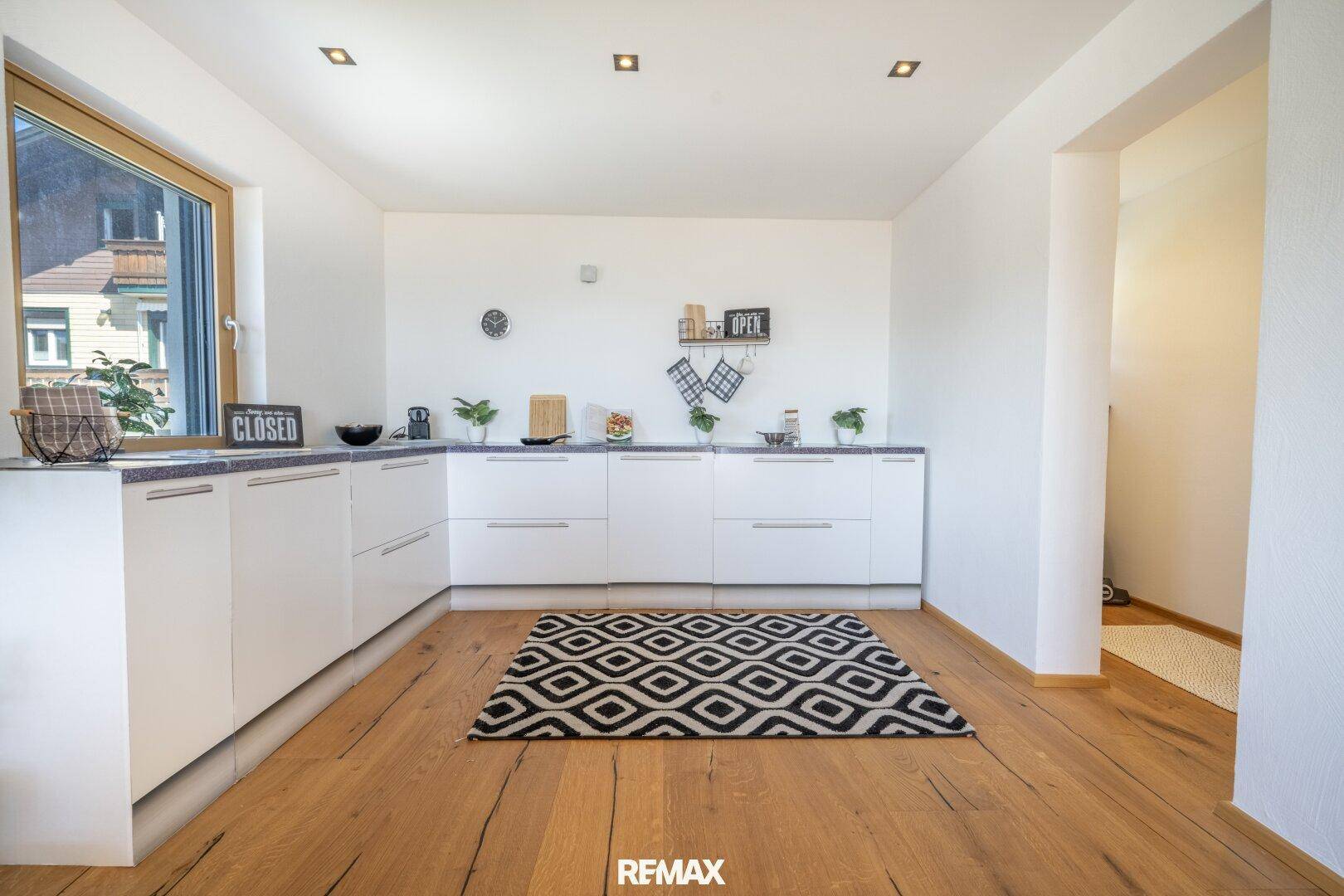 Helle, moderne Küche mit weißen Schränken, Holzboden und Fenster.