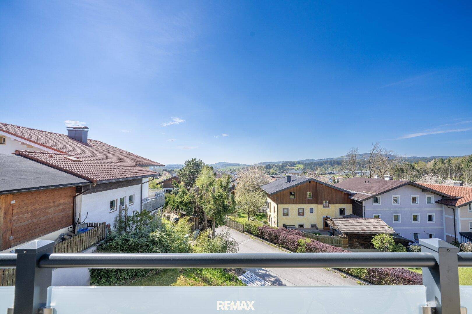 Weitläufiger Blick über eine Wohnsiedlung mit Häusern und grüner Landschaft unter blauem Himmel.