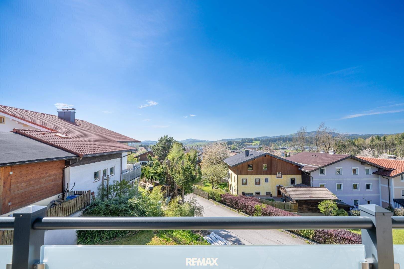 Weitläufiger Blick über eine Wohnsiedlung mit Häusern und grüner Landschaft unter blauem Himmel.