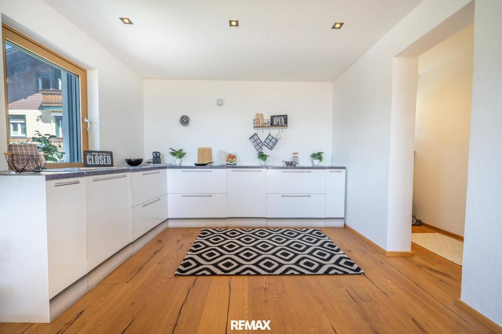 Helle, moderne Küche mit weißen Schränken, Holzboden und Fenster.