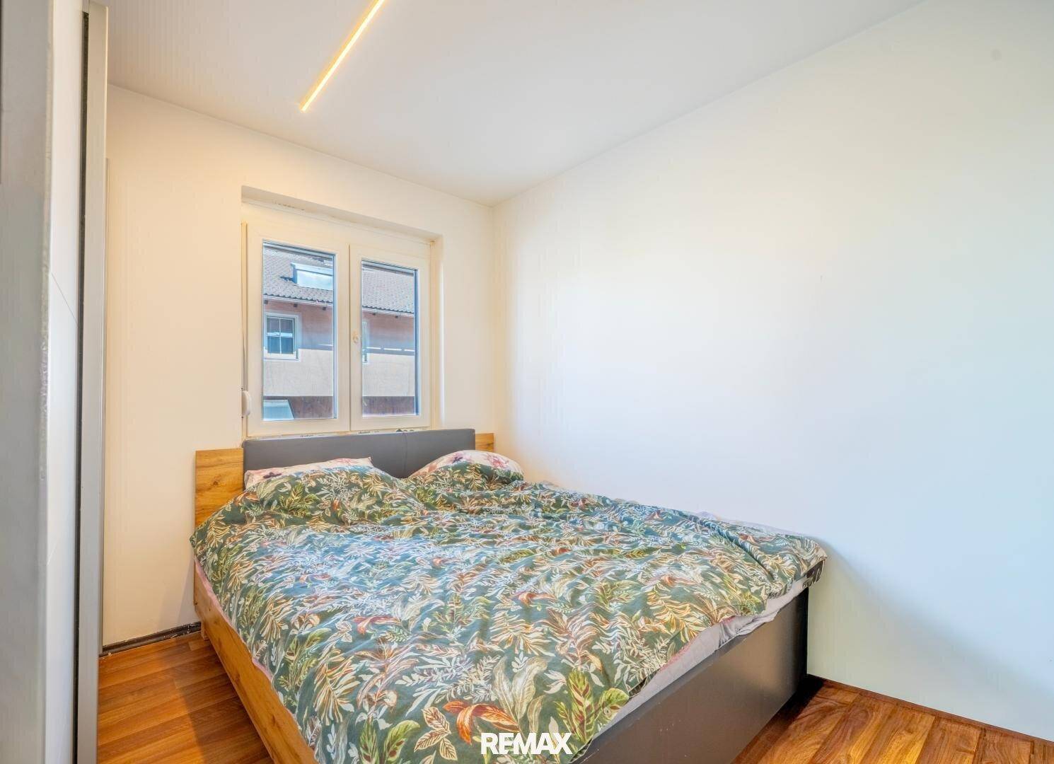 Helles Schlafzimmer mit Doppelbett, Laminatboden und einem Fenster.