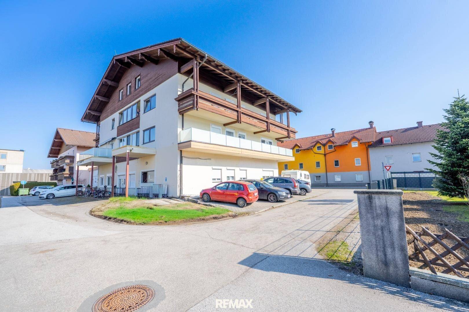 Mehrfamilienhaus mit traditioneller Architektur, Balkonen und Parkplätzen im Freien.