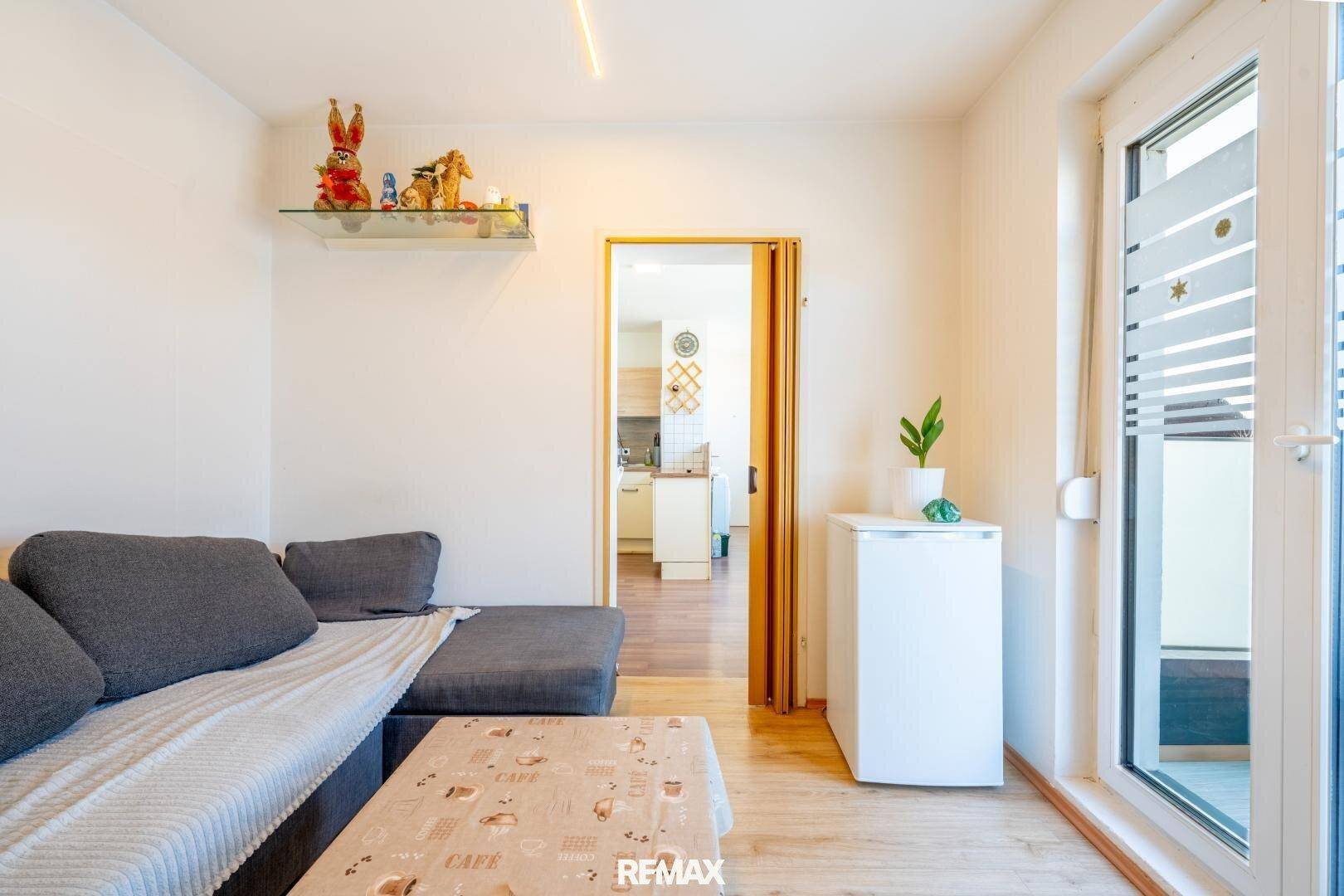 Gemütliches Wohnzimmer mit Sofa, Laminatboden und Blick in die angrenzende Küche.