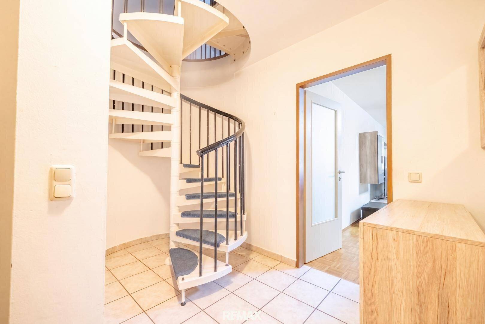 Heller Flur mit Wendeltreppe, Fliesenboden und einer Holzkommode.