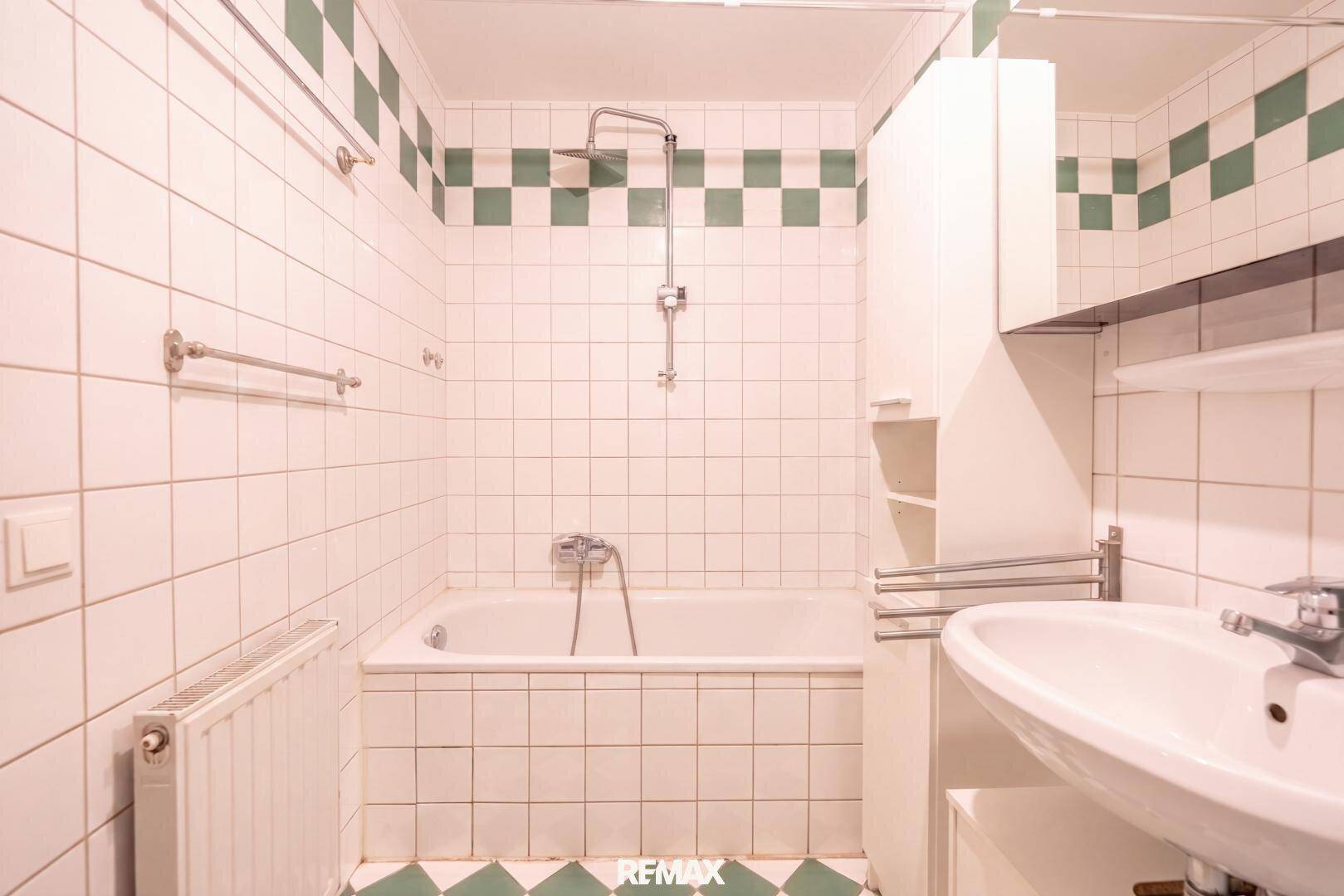 Badezimmer mit Badewanne, Dusche, Waschbecken und grün-weiß karierten Fliesen.