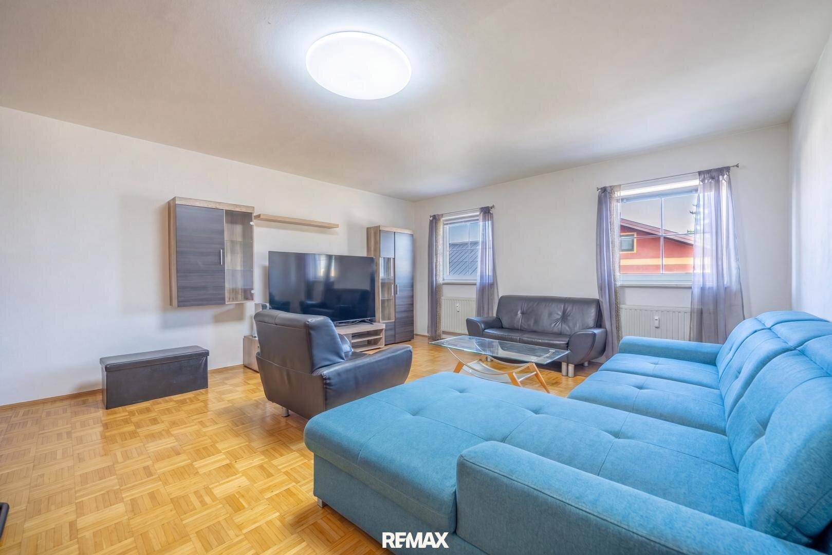 Gemütliches Wohnzimmer mit blauer Couch, Fernseher und Parkettboden.