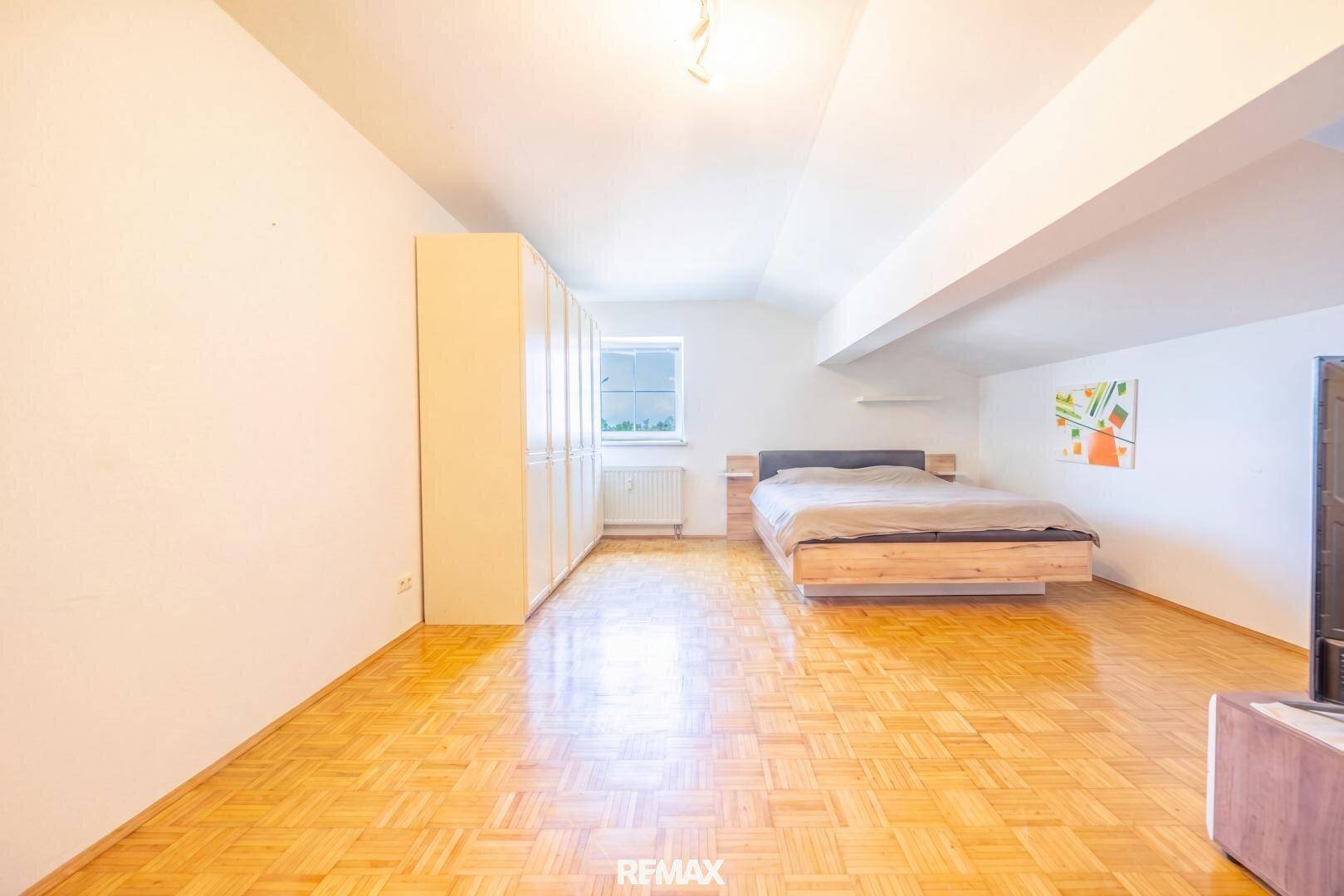 Helles Schlafzimmer mit Parkettboden, großem Kleiderschrank und einem Fenster.