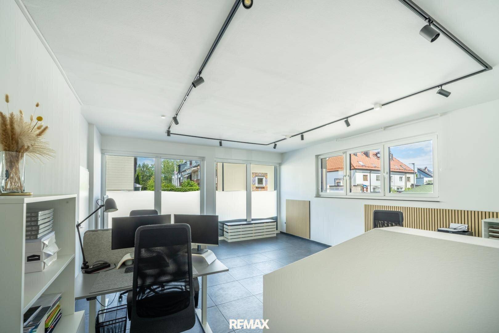 Modernes Büro mit Arbeitsplätzen, großen Fenstern und einem Regal mit Büchern und Dekoration.