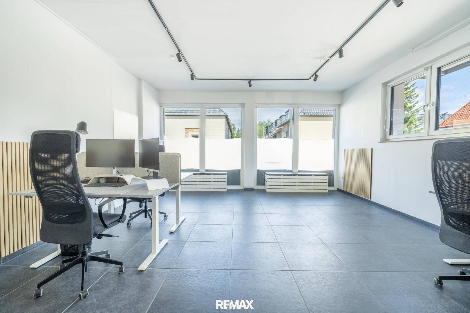 Helles Büro mit mehreren Arbeitsplätzen, großen Fenstern und einer Holzlamellenwand.