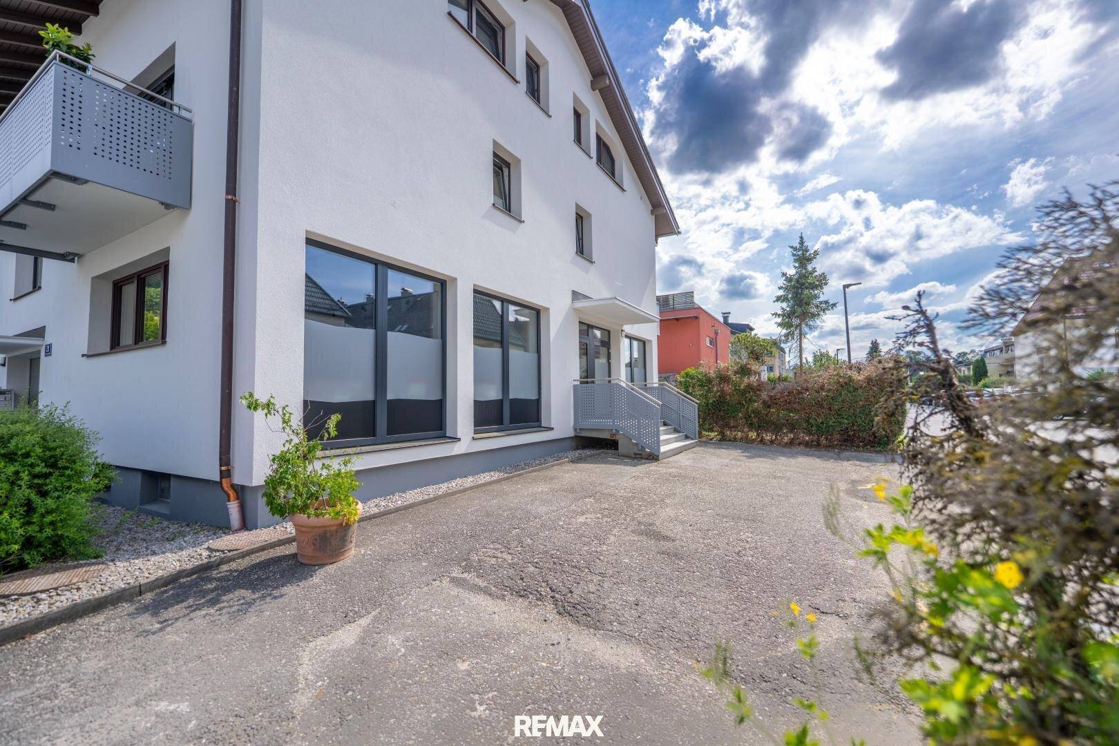 Seitenansicht des weißen Gebäudes mit Balkon, Einfahrt und gepflegter Hecke im Vordergrund.