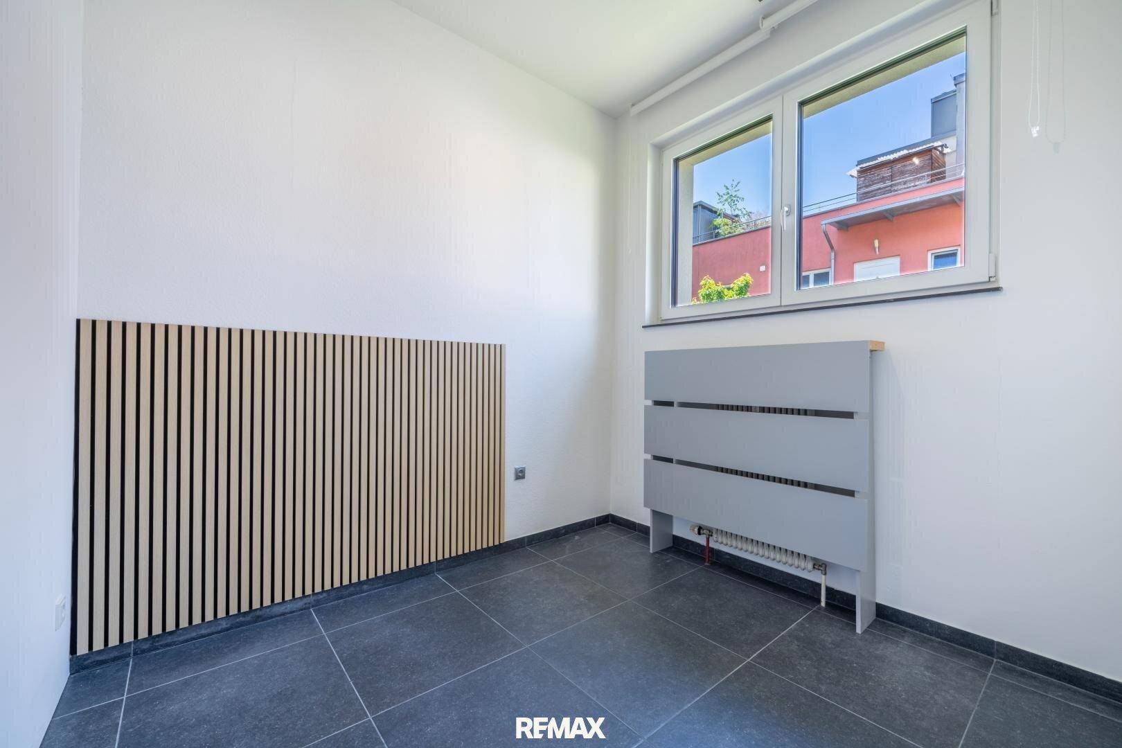 Heller Büroraum mit dunklen Fliesen, einem Fenster und einer dekorativen Holzlamellenwand.