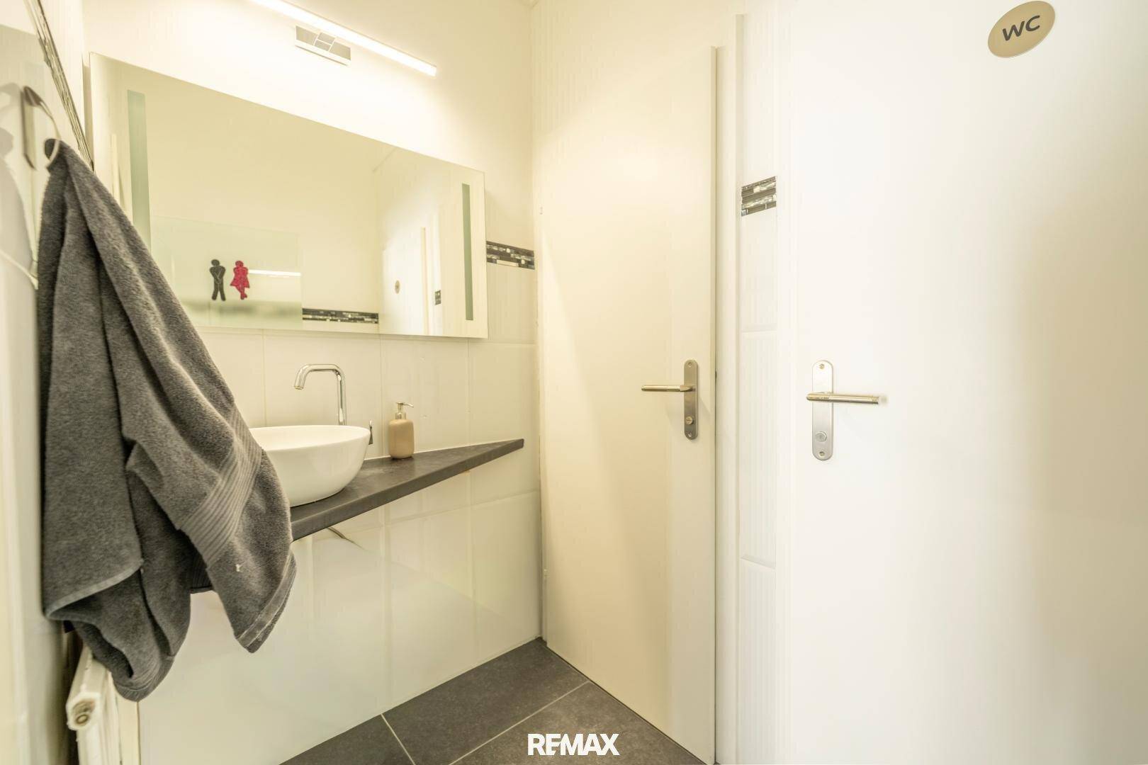 Modernes Gäste-WC mit Waschbecken, Spiegel und dunklem Fliesenboden.