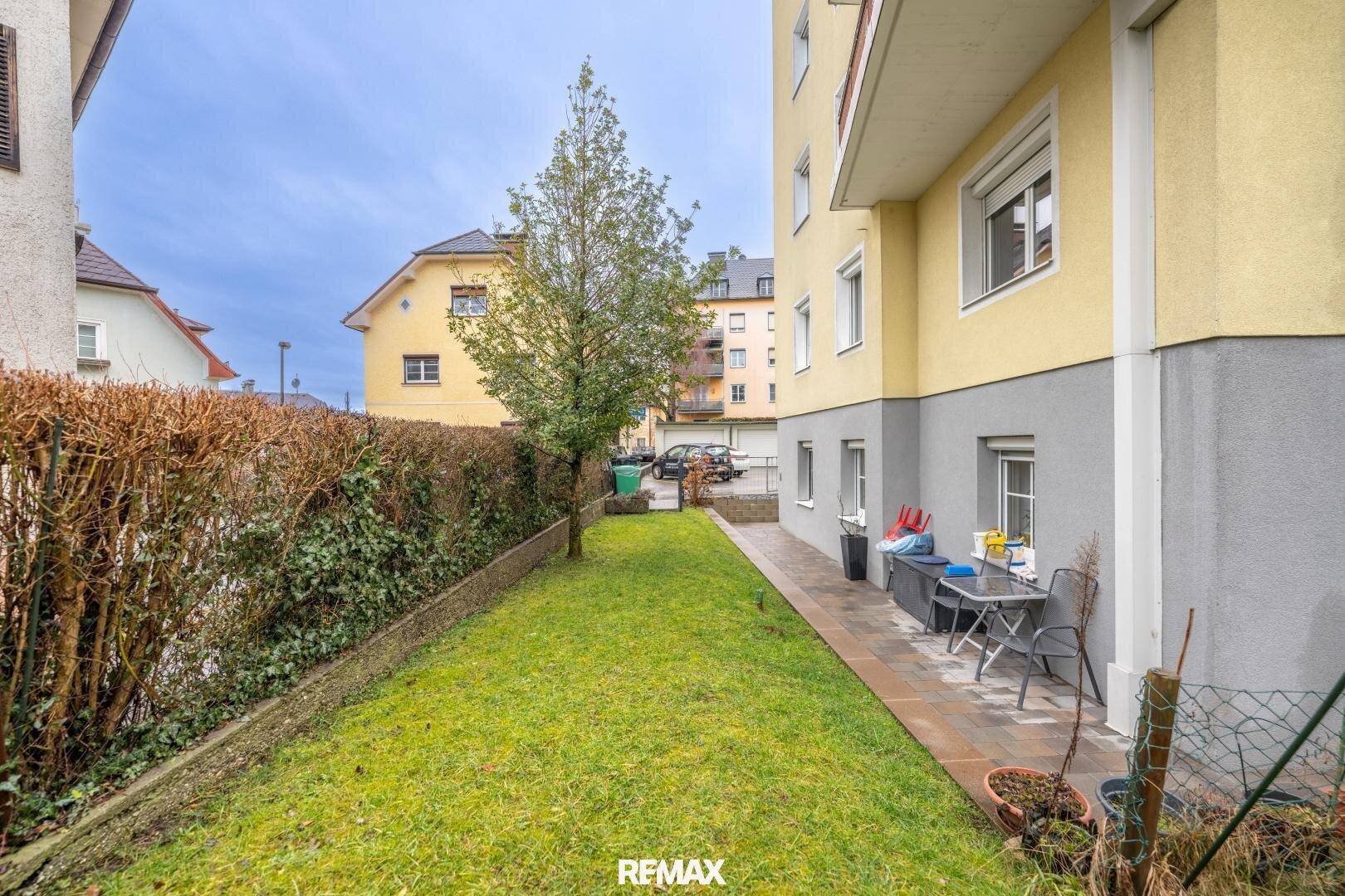 Seitlicher Gartenbereich mit Rasen, Hecke und kleiner Terrasse am Haus.