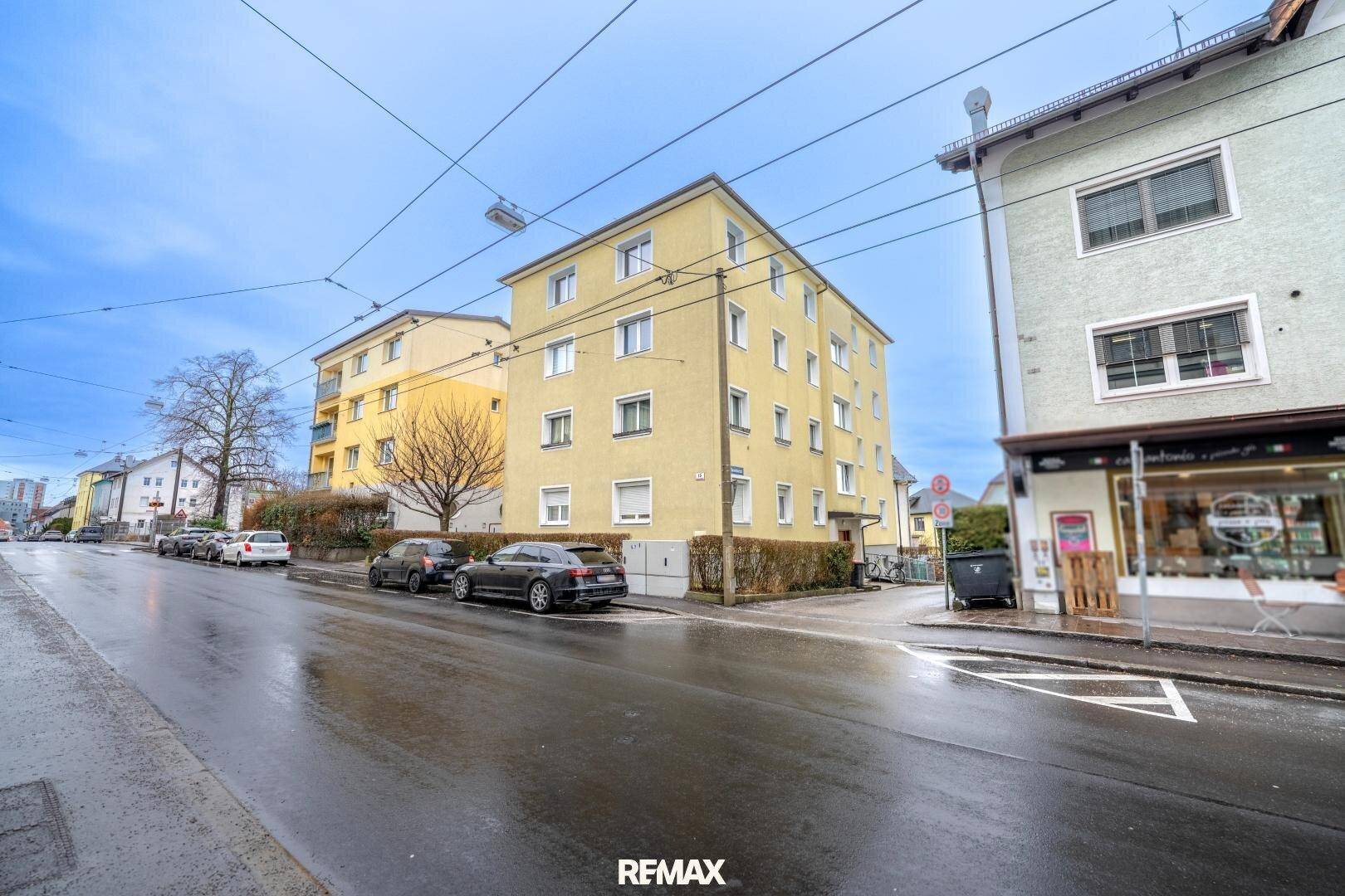 Mehrfamilienhaus mit gelber Fassade an einer städtischen Straße mit parkenden Autos.