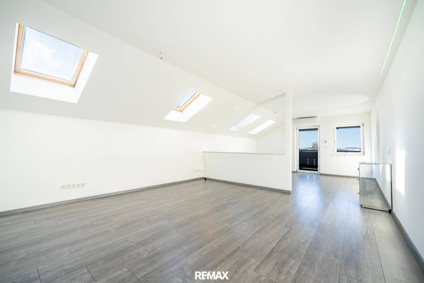 Offener Wohnbereich im Dachgeschoss mit vielen Dachfenstern und Zugang zu einem Balkon.