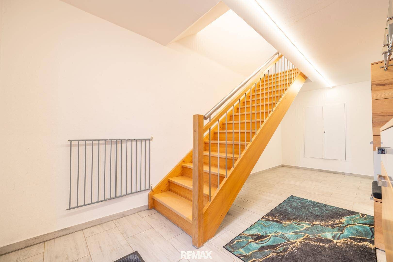 Holztreppe mit Metallgeländer, die in ein helles Obergeschoss führt, mit modernem Teppich.