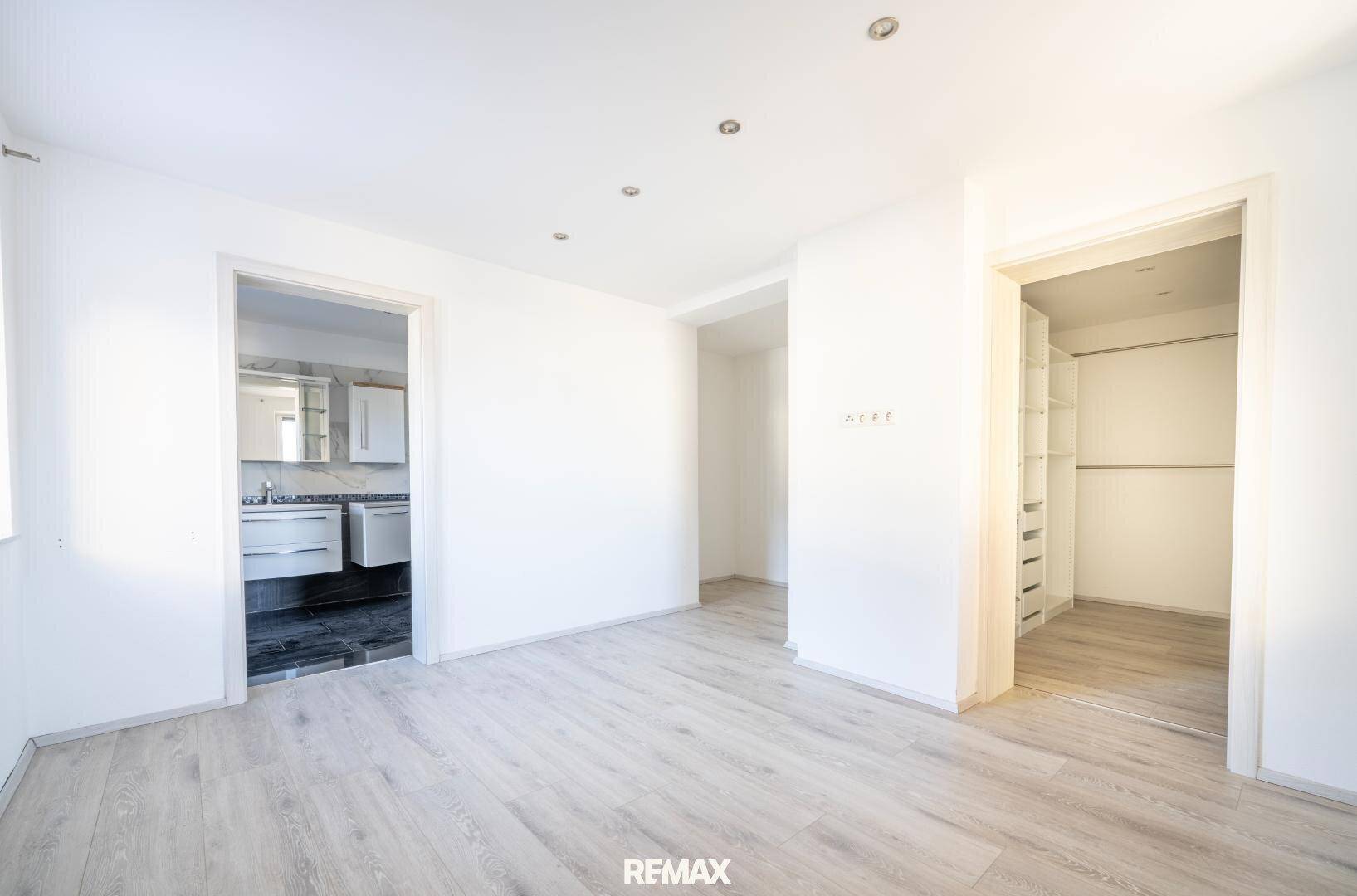 Geräumiger Raum mit hellem Laminatboden, der zu einem Badezimmer und einem begehbaren Kleiderschrank führt.