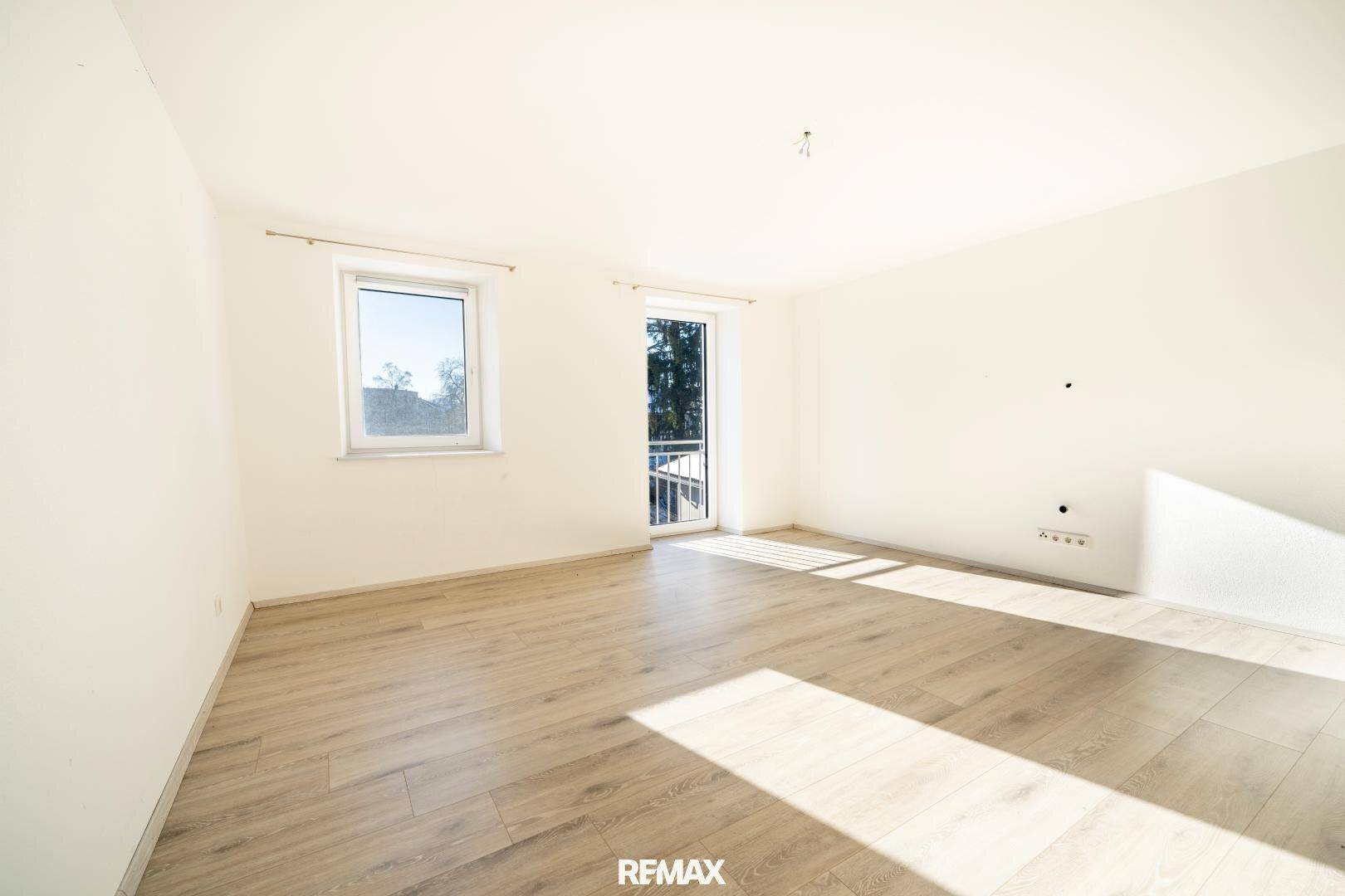 Heller Raum mit Laminatboden, großem Fenster und Zugang zu einem französischen Balkon.