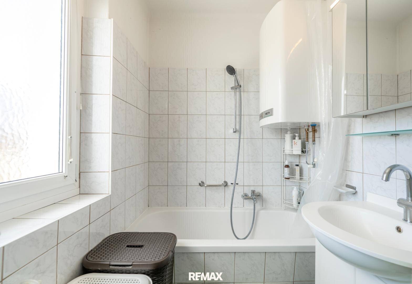 Helles Badezimmer mit Badewanne, Dusche und Fenster für natürliche Belüftung.