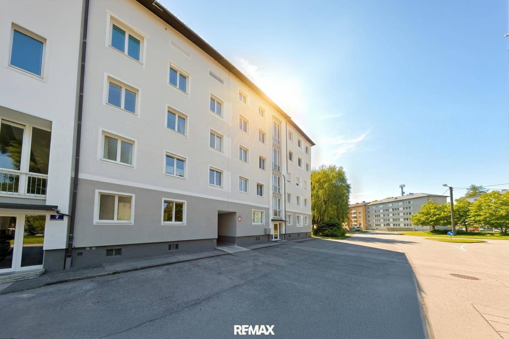 Mehrfamilienhaus mit moderner Fassade und sonnigem Außenbereich am Tag.