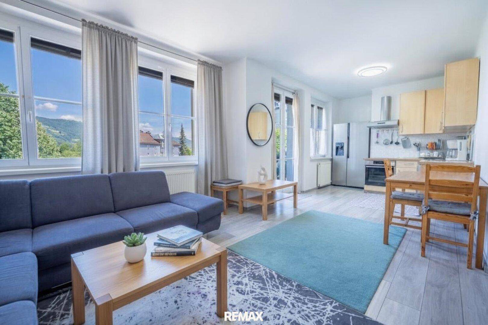 Heller offener Wohn- und Essbereich mit Sofa, Teppich und integrierter Küche mit Bergblick.