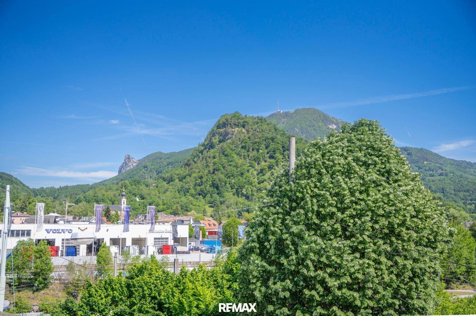 Panoramablick auf grüne Berge und die umliegende Bebauung unter strahlend blauem Himmel.