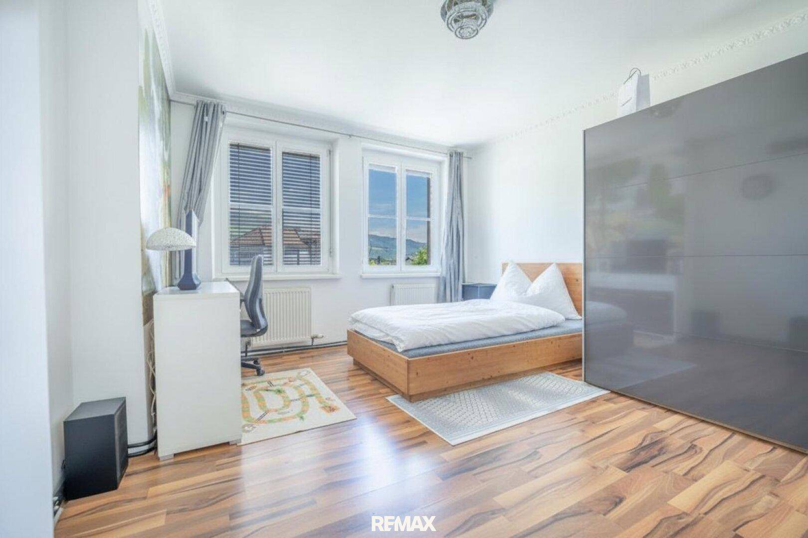 Helles Schlafzimmer mit Holzbett, Schreibtisch und großem Kleiderschrank mit Bergblick.