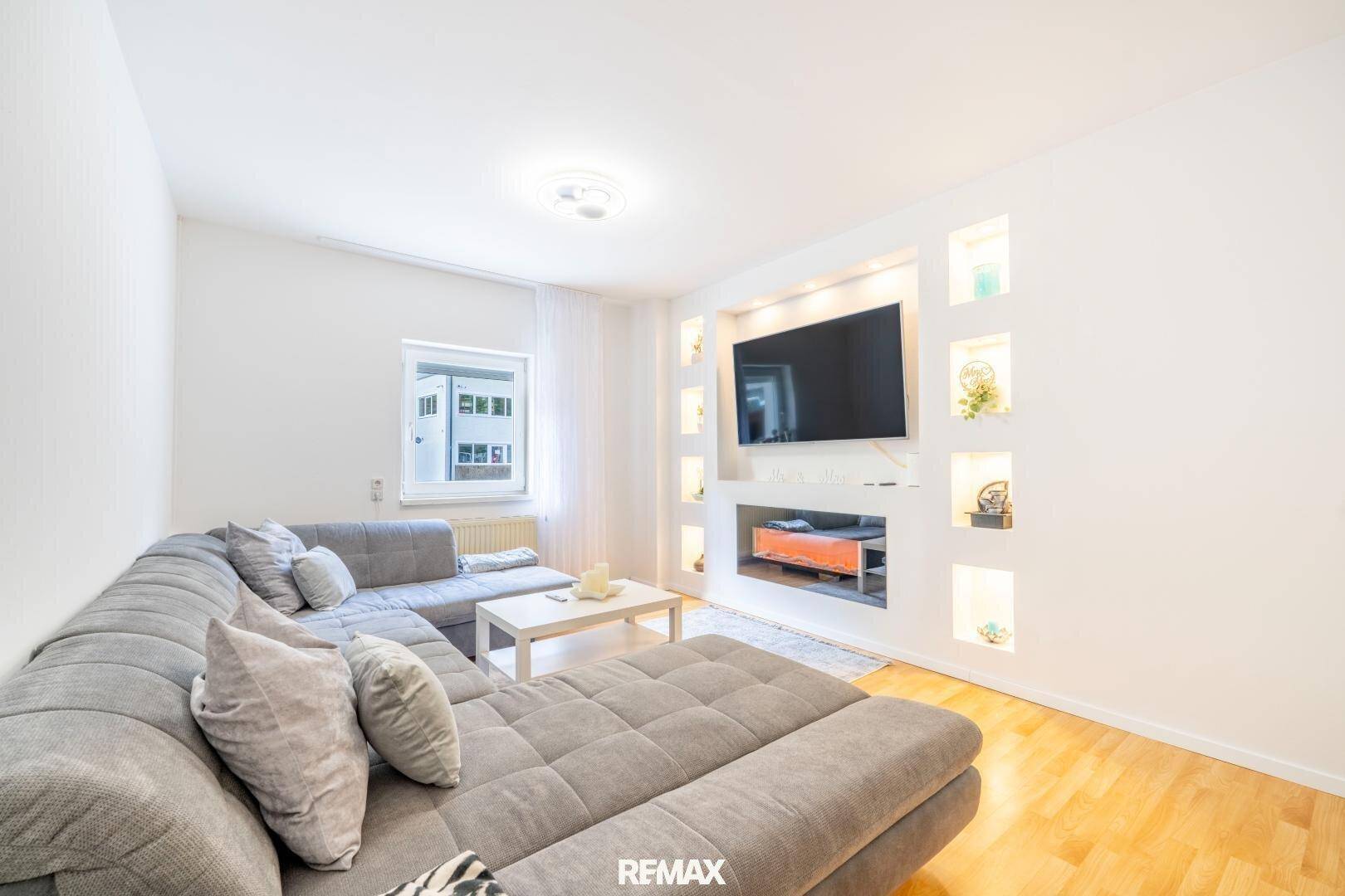 Gemütliches Wohnzimmer mit großem Ecksofa, Wandfernseher und dekorativen Nischen.