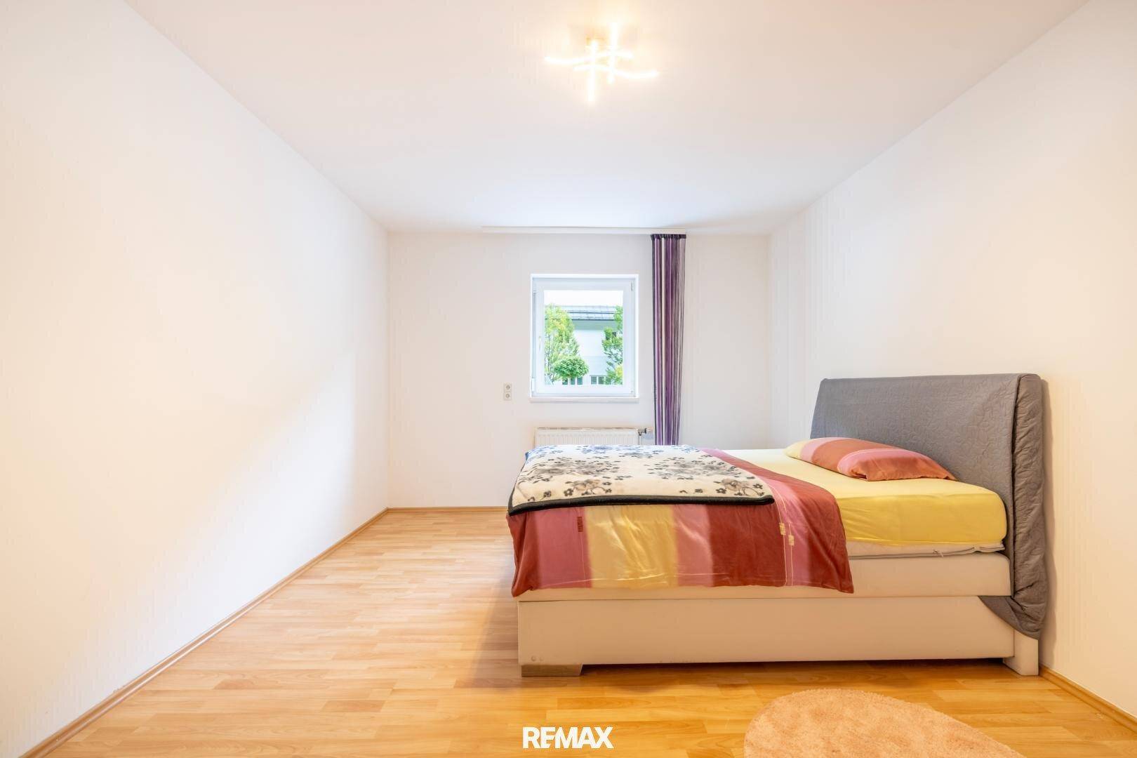 Helles Schlafzimmer mit Holzboden, großem Bett und Blick ins Grüne.